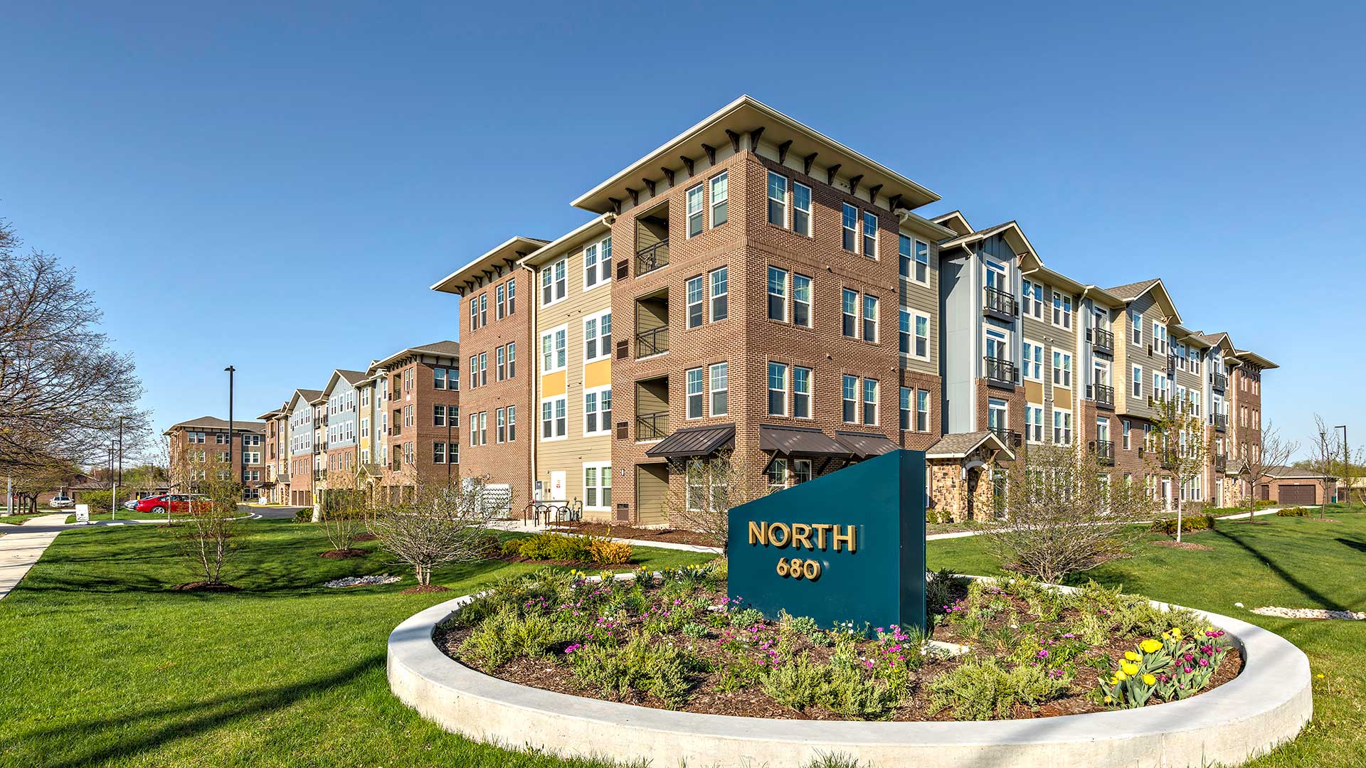 The main entrance sign for North 680 is blue with an angled top and North 680 in gold lettering. The apartment building is seen behind on a clear day.