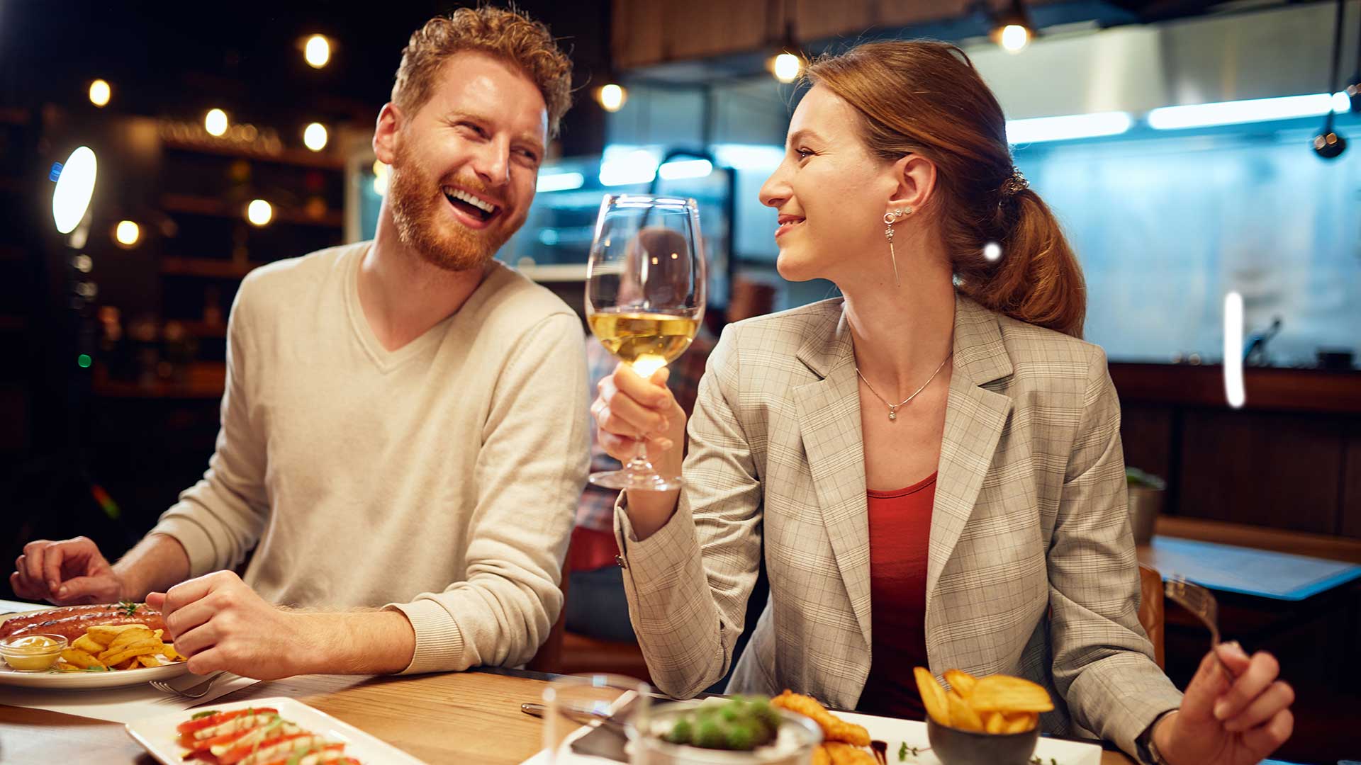 Smiling couple in a restaurant, having dinner and talking. The man is talking to the woman while a woman listening to him and drinking white wine.