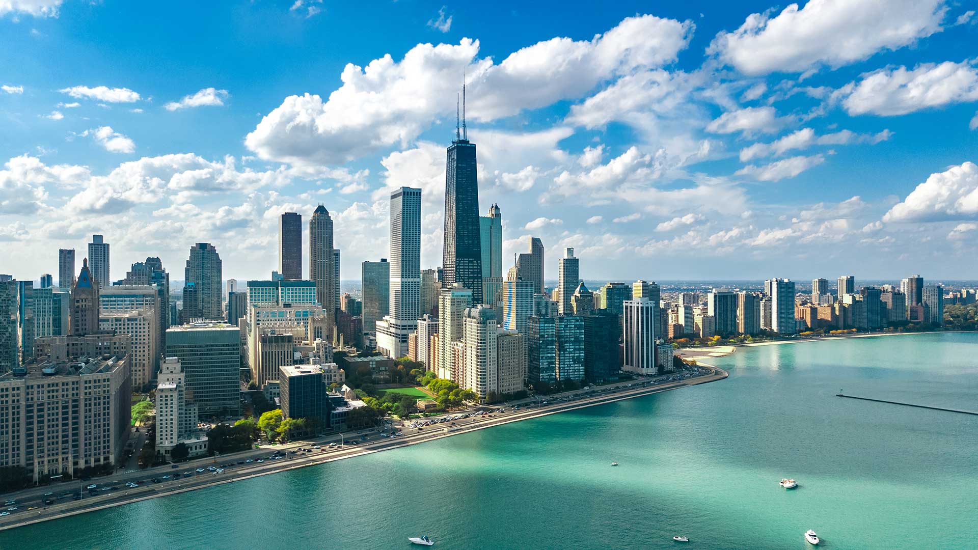 The Chicago skyline as seen from a drone over Lake Michigan on a partially cloudy day.
