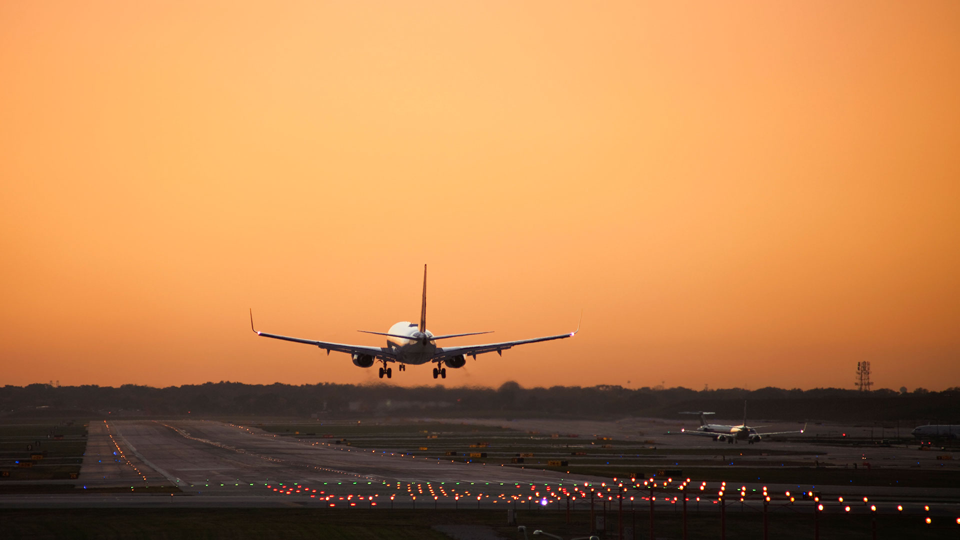 A plane just about to land on a runway at dusk: the sky is entirely orange.